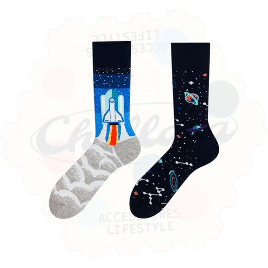 Chaussettes fantaisie dépareillées motif espace : une chaussette avec fusée au décollage sur fond nuageux et bleu, l’autre avec constellations, planètes et galaxies sur fond noir.